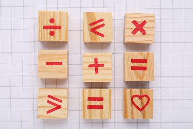Wooden cubes with mathematical symbols and heart on sheet of grid paper, flat lay