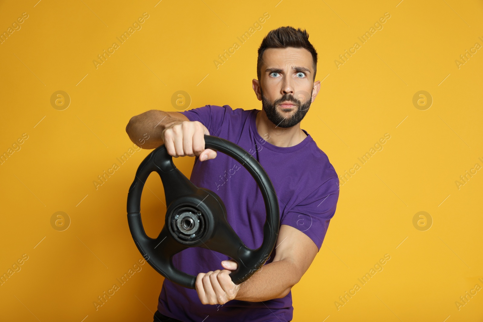 Photo of Serious man with steering wheel on yellow background