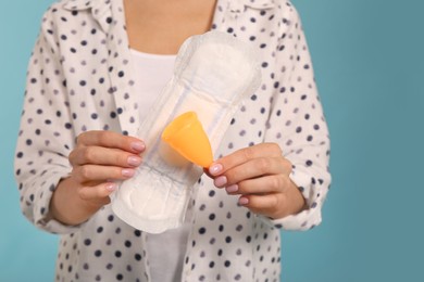 Young woman with menstrual cup and pad on light blue background, closeup