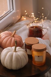 Beautiful pumpkins and scented candles on window sill indoors