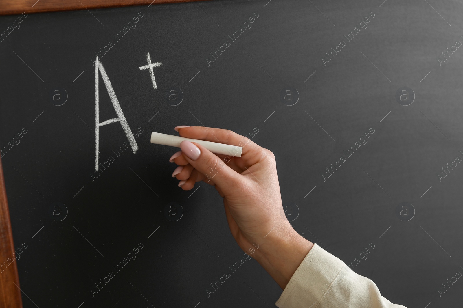 Photo of School grade. Teacher writing letter A and plus symbol with chalk on blackboard, closeup