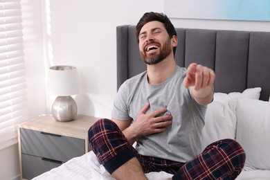 Photo of Handsome man pointing at something and laughing in bedroom. Space for text