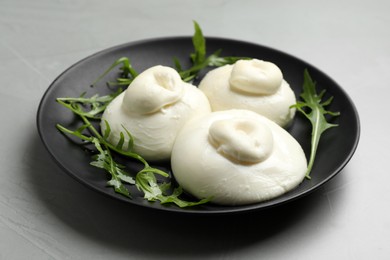 Photo of Delicious burrata cheese with arugula on light grey table, closeup