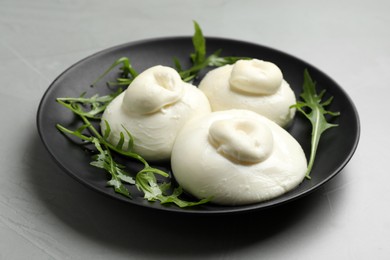 Delicious burrata cheese with arugula on light grey table, closeup