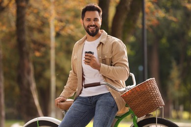 Photo of Young man with bicycle holding takeaway coffee in autumn park