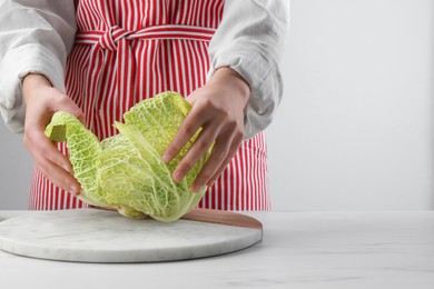 Photo of Woman separating leaf from fresh savoy cabbage at white marble table, closeup