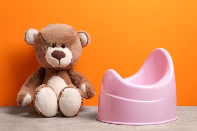 Photo of Teddy bear and pink baby potty on stone table against orange background. Toilet training