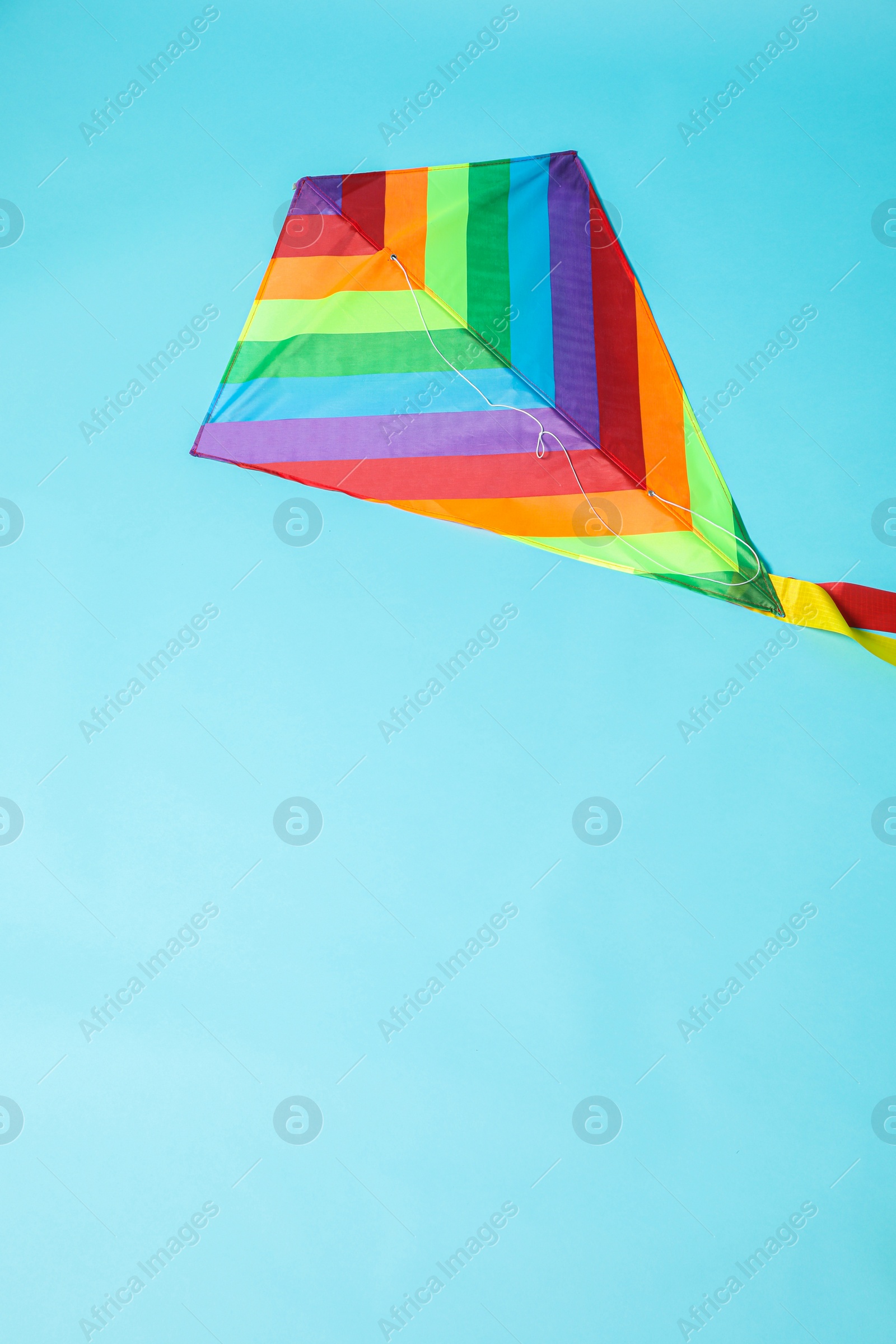 Photo of Bright rainbow kite on light blue background, top view. Space for text