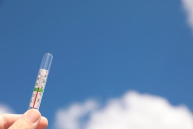 Photo of Woman holding weather thermometer against blue sky, closeup. Space for text