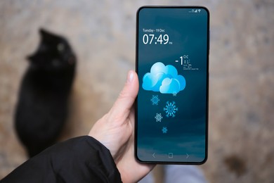 Image of Woman checking weather using app on smartphone outdoors, closeup. Data and illustration of cloud with snowflakes on screen