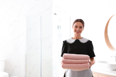 Photo of Young chambermaid holding stack of fresh towels in bathroom. Space for text