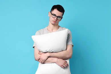 Photo of Man in pyjama holding pillow on light blue background