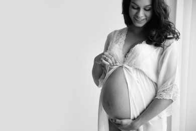 Young pregnant woman in lace nightgown on light background, black and white effect. Space for text