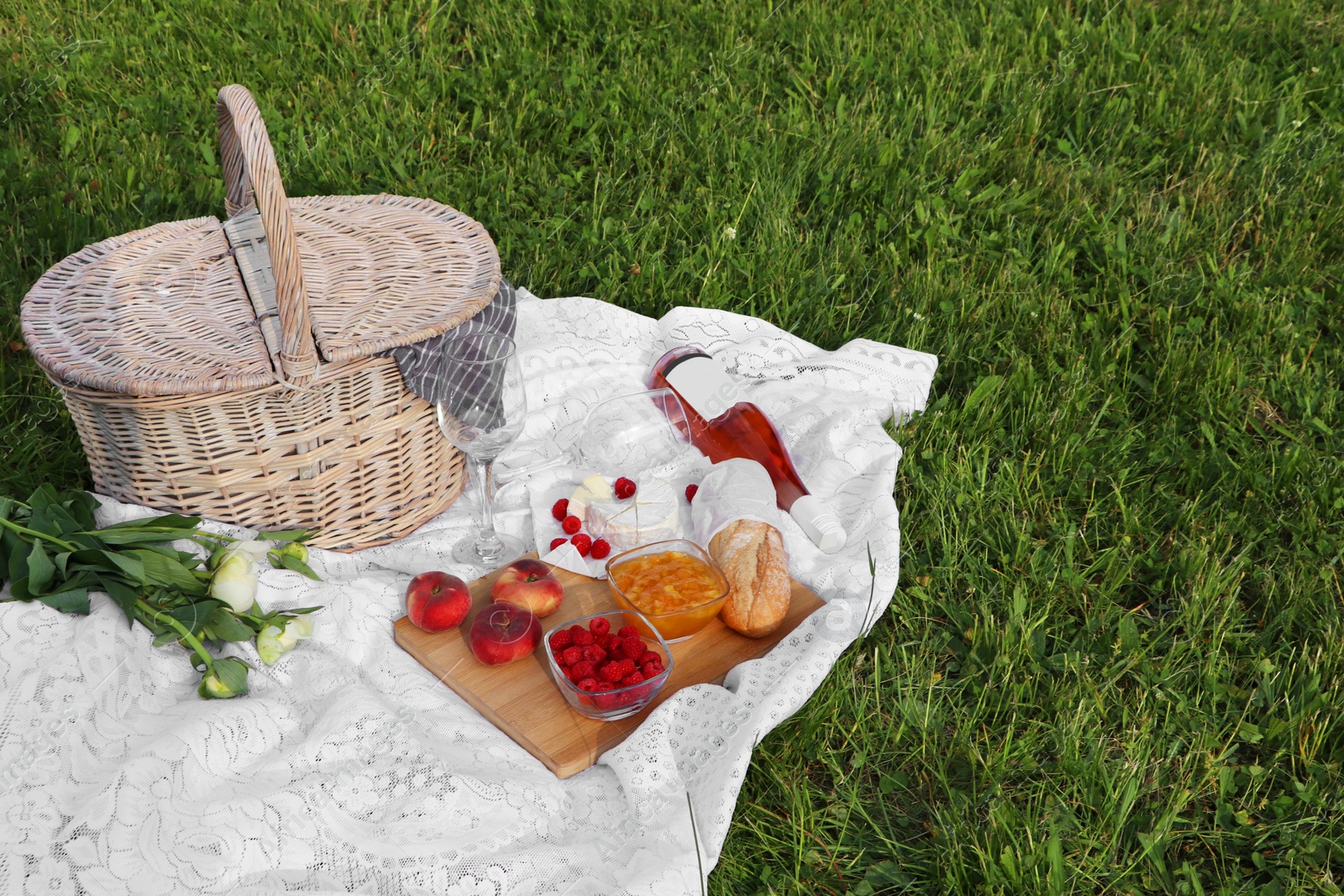 Photo of Picnic blanket with tasty food, flowers, basket and cider on green grass outdoors. Space for text