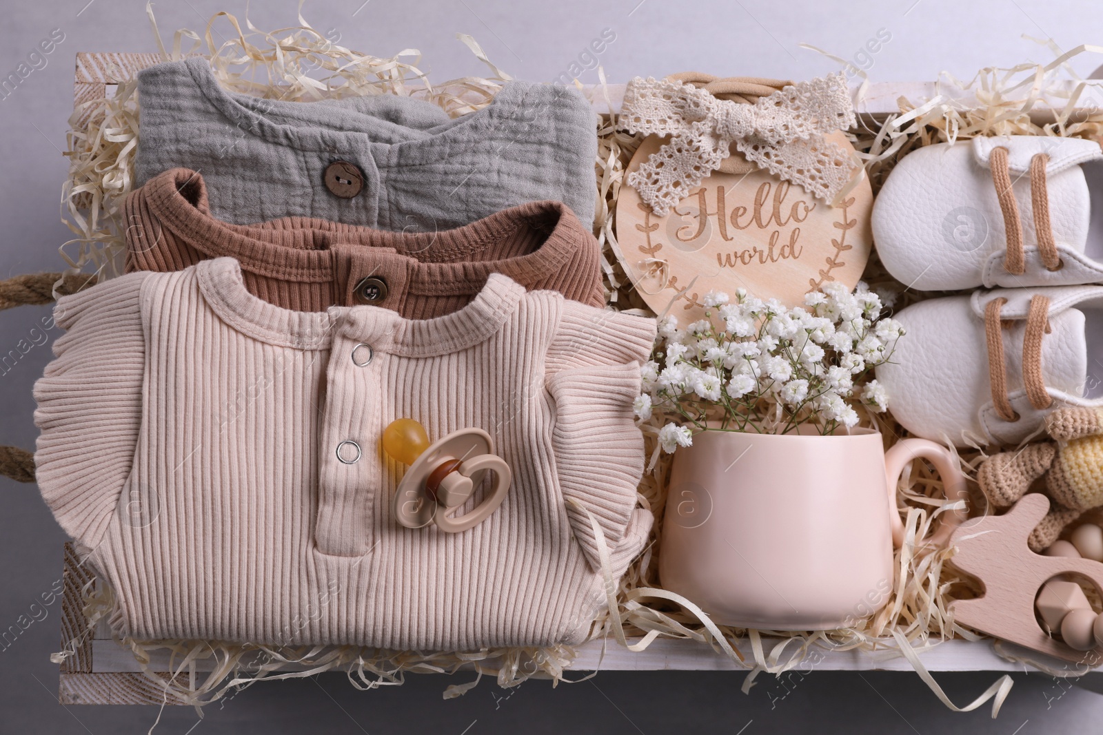 Photo of Wooden box with baby clothes, booties and toys on grey background, top view