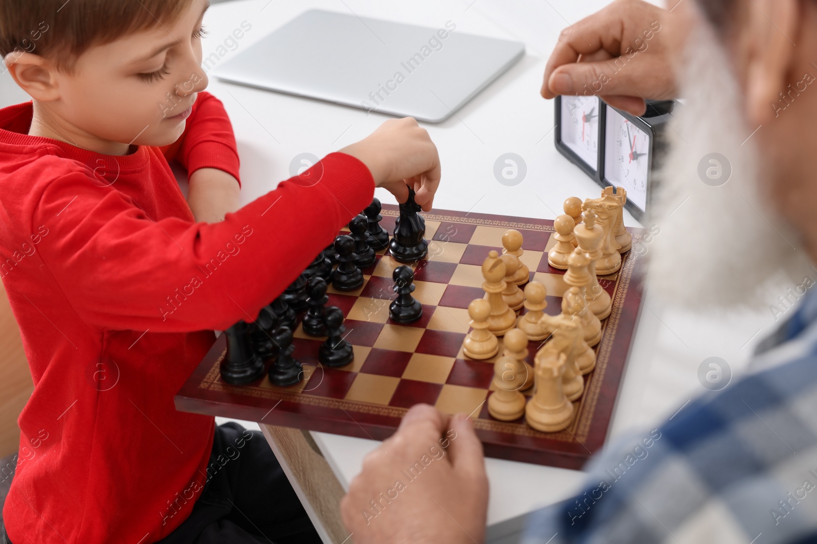 Photo of Grandfather and grandson playing chess at table indoors, closeup