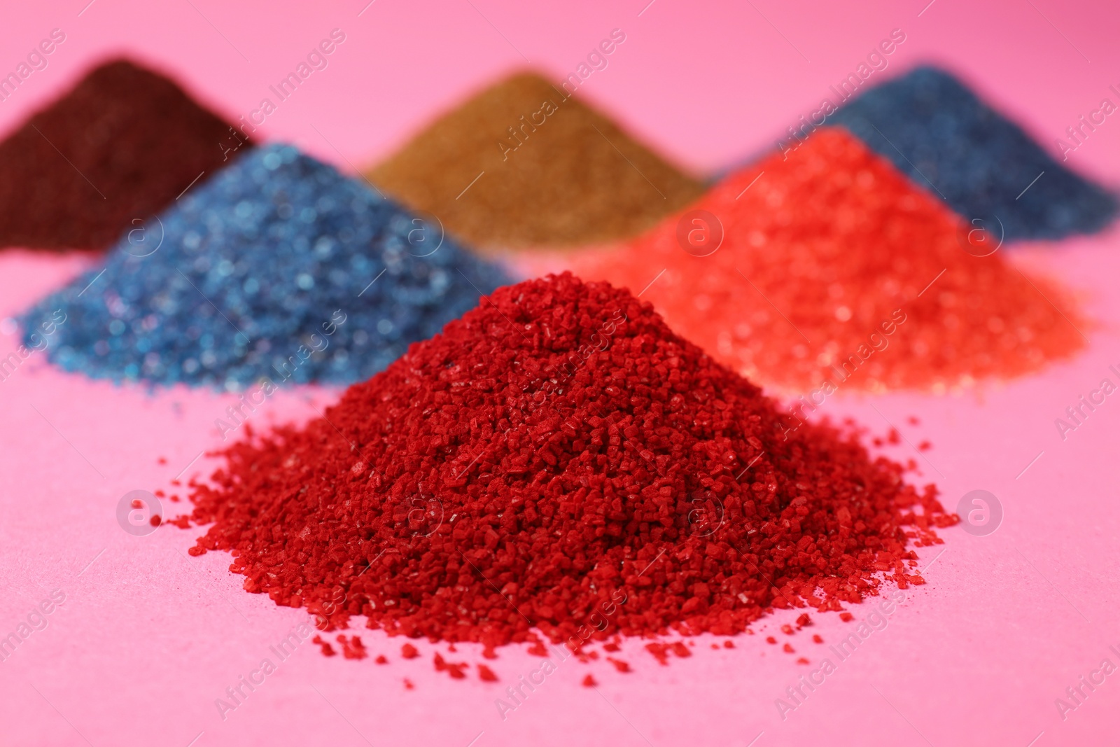 Photo of Heaps of different bright food coloring on pink background, closeup
