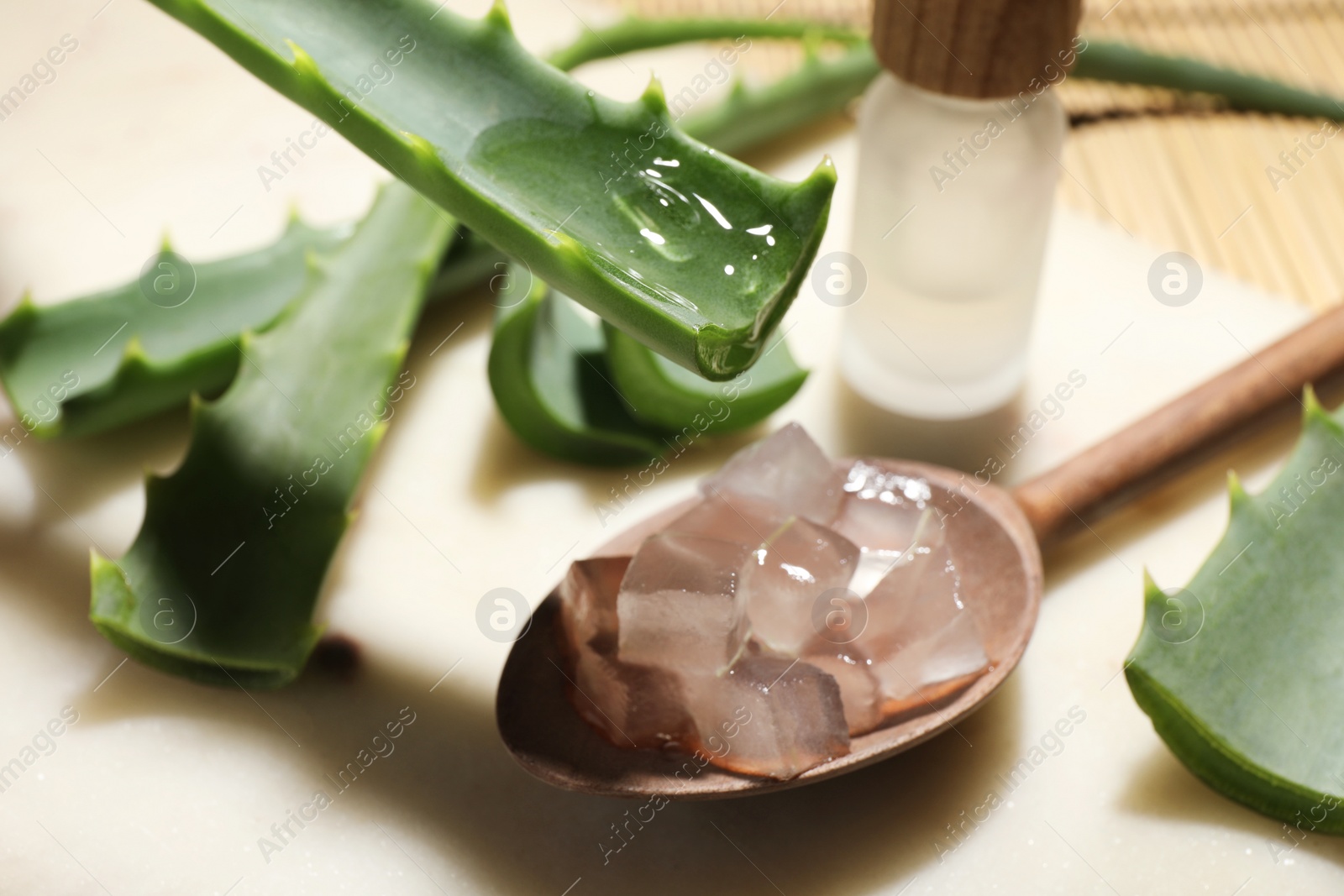 Photo of Dripping aloe vera gel from leaf into spoon at light table, closeup