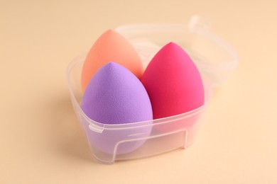 Photo of Many different makeup sponges in plastic container on beige background, closeup