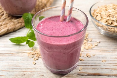 Photo of Glass of blackberry smoothie with straws, mint and oatmeal on light wooden table, closeup
