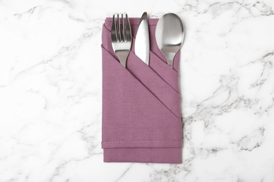 Photo of Folded napkin with fork, spoon and knife on marble background, top view