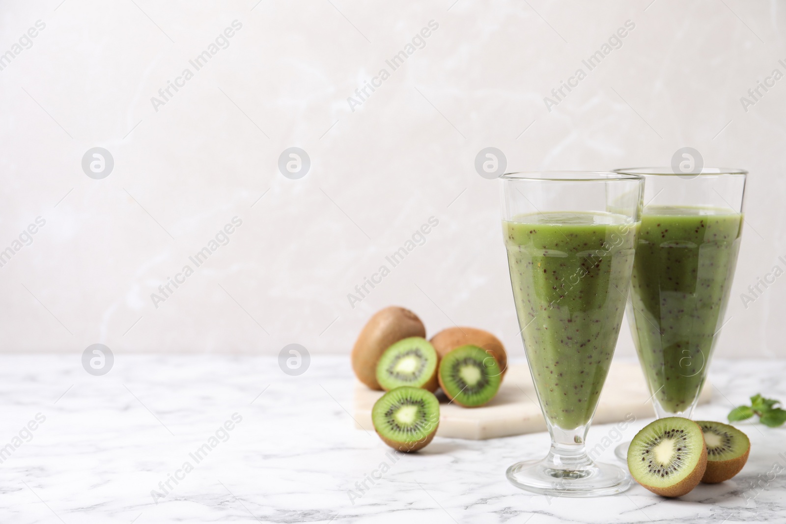 Photo of Delicious kiwi smoothie and fresh fruits on white marble table. Space for text