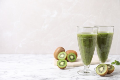 Delicious kiwi smoothie and fresh fruits on white marble table. Space for text