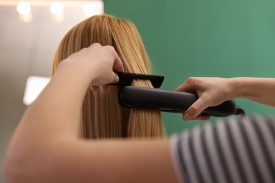 Stylist straightening woman's hair with flat iron in salon