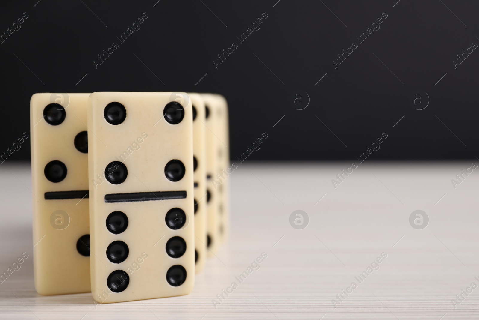 Photo of Domino tiles on wooden table against black background, closeup. Space for text