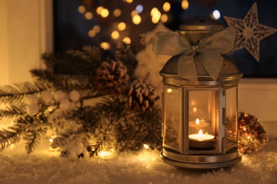 Beautiful Christmas lantern and other decorations on snowy window sill at night