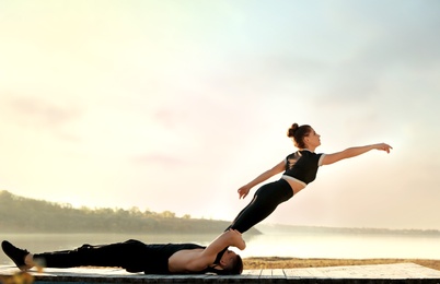 Photo of Beautiful young couple practicing dance moves near river at sunset