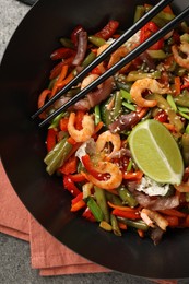 Shrimp stir fry with vegetables in wok and chopsticks on grey table, top view