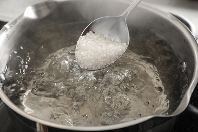 Salting boiling water in pot on stove, closeup