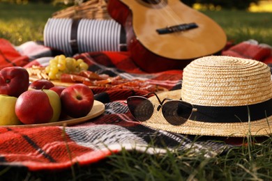 Photo of Straw hat, glasses and different snacks for summer picnic on plaid outdoors
