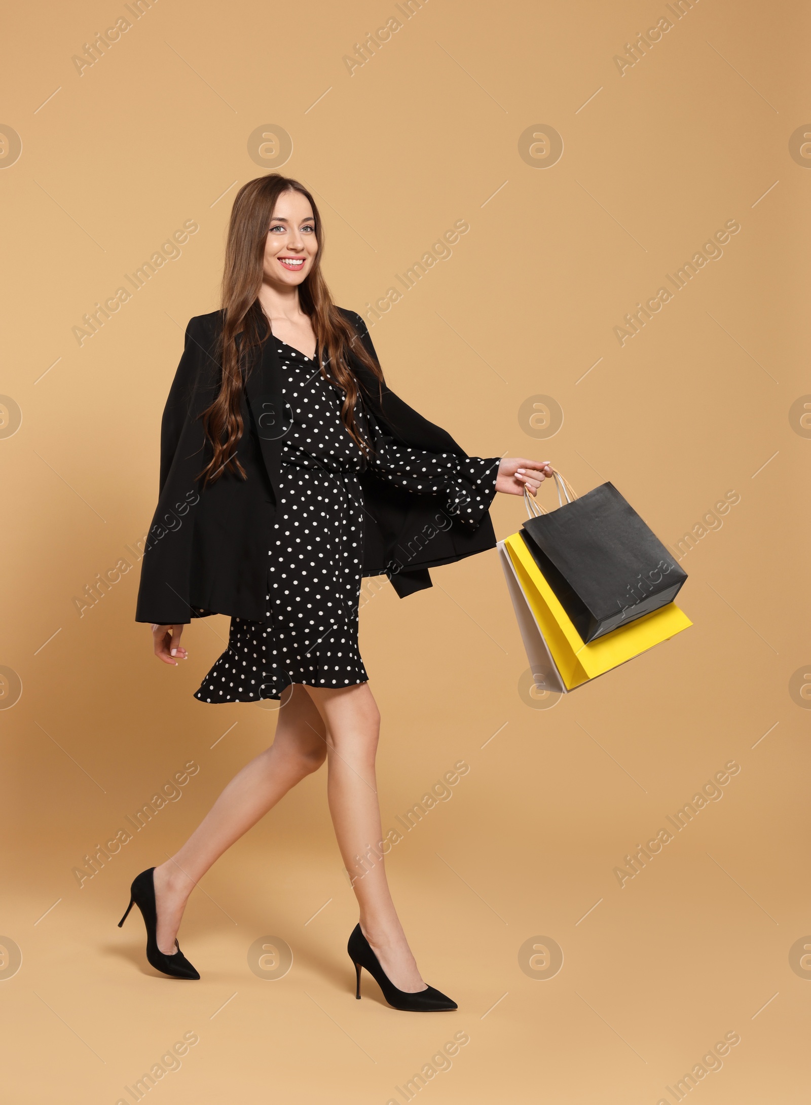 Photo of Stylish young woman with shopping bags on beige background
