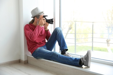 Male photographer with professional camera on window sill indoors