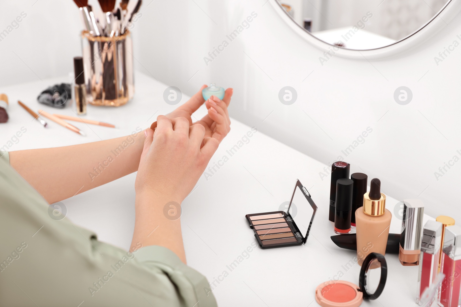 Photo of Woman applying perfume on wrist at dressing table indoors, closeup
