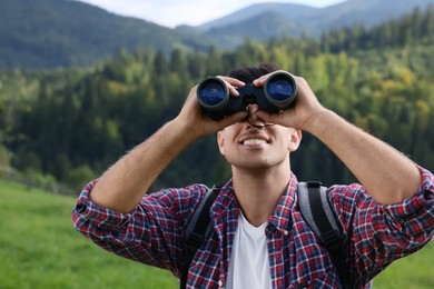 Photo of Man with backpack looking through binoculars in mountains