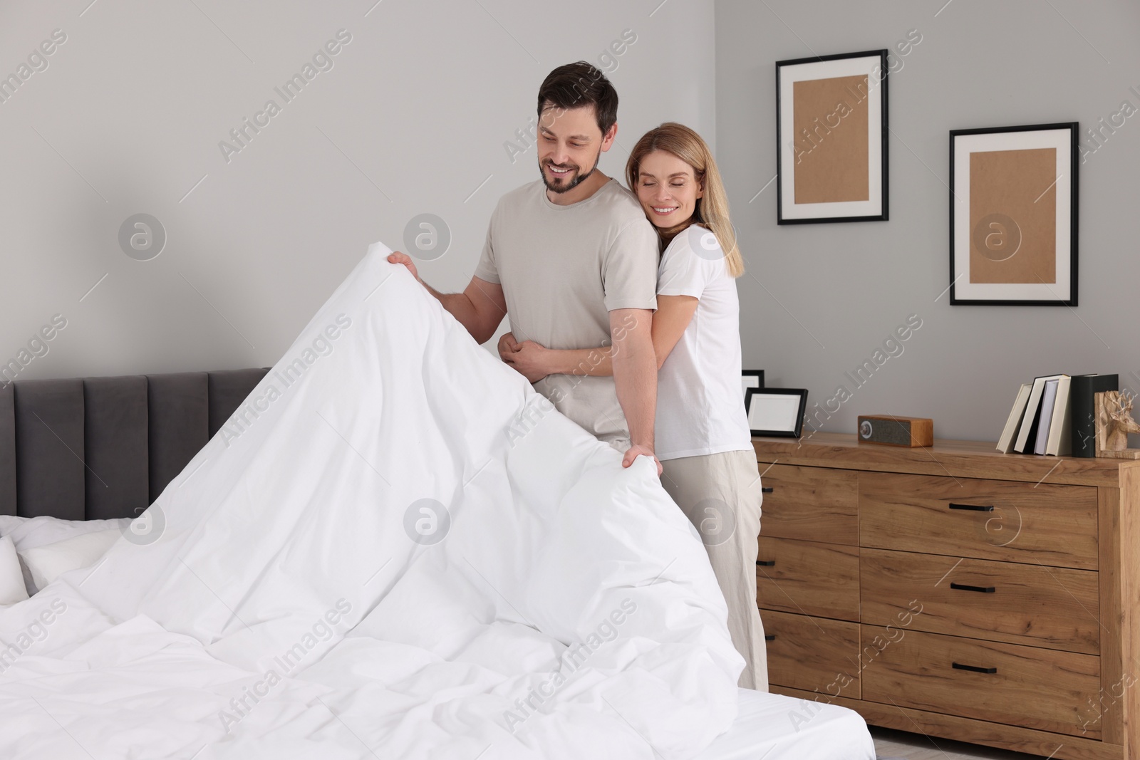 Photo of Couple changing bed linens in room. Domestic chores