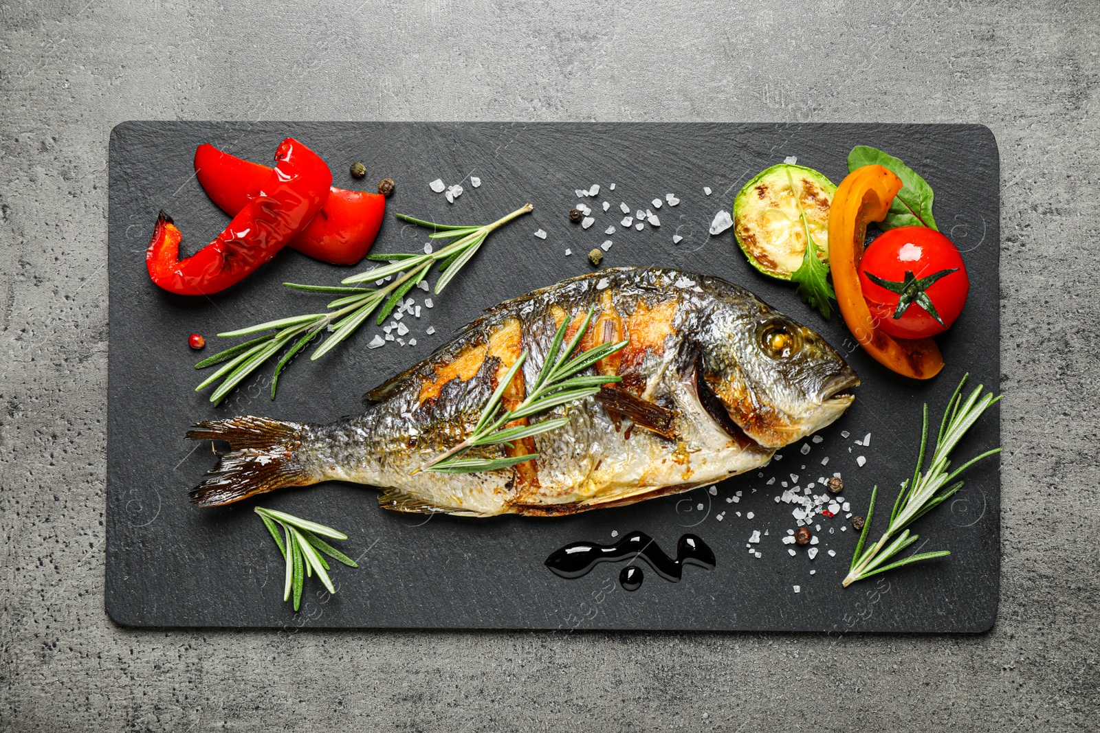 Photo of Delicious roasted fish and vegetables on grey table, flat lay