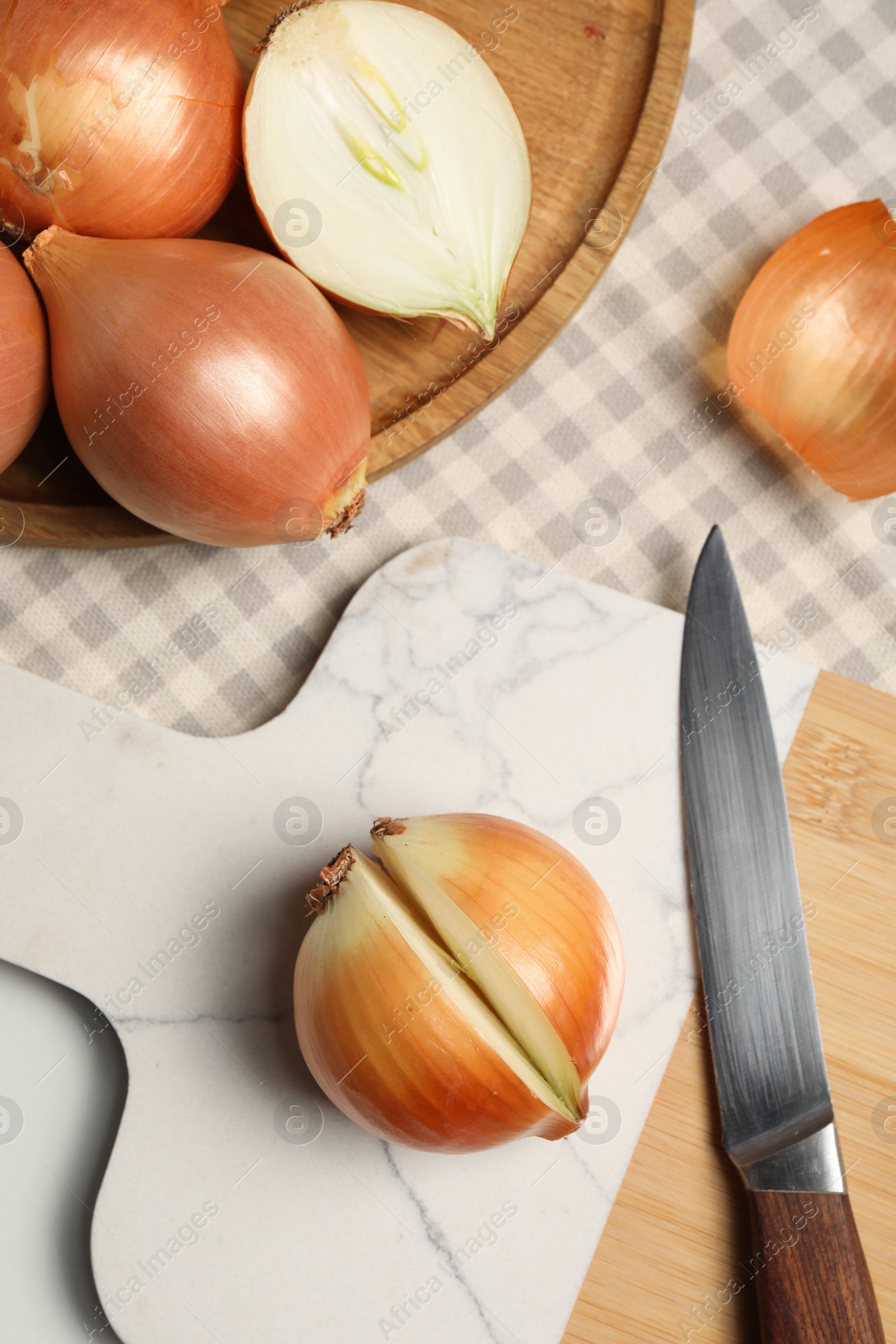 Photo of Whole and cut onions with knife on white table, flat lay