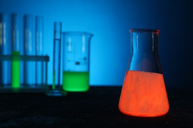 Photo of Laboratory glassware with luminous liquids on table against light blue background, selective focus. Space for text