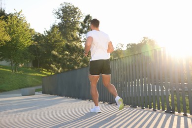 Photo of Man running outdoors on sunny day, back view. Space for text