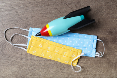 Photo of Homemade protective masks and toy rocket on wooden background, flat lay. Sewing for child