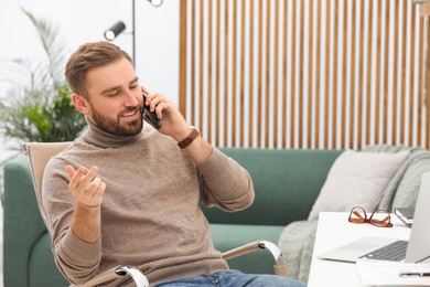 Photo of Young man talking on phone while working at home, space for text