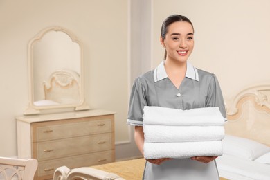 Photo of Young chambermaid holding stack of clean towels in hotel room. Space for text