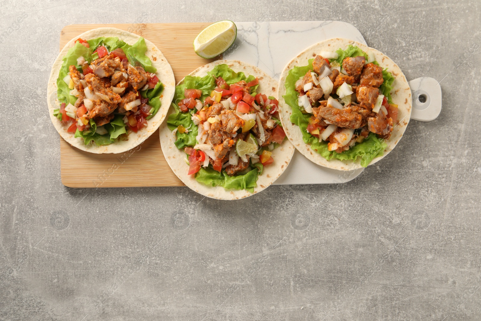 Photo of Delicious tacos with vegetables, meat and lime on grey textured table, top view. Space for text