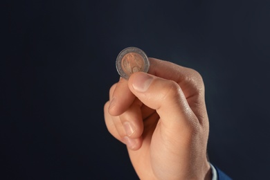 Young man holding coin on dark background, closeup