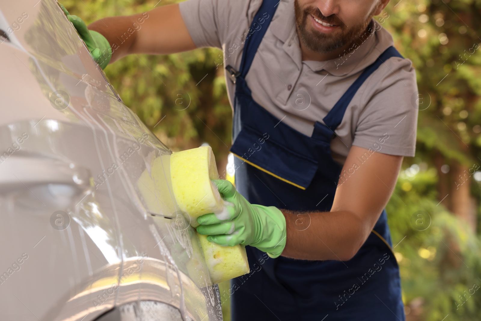 Photo of Worker washing auto with sponge at outdoor car wash, closeup