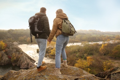 Couple of hikers with travel backpacks near mountain river, back view